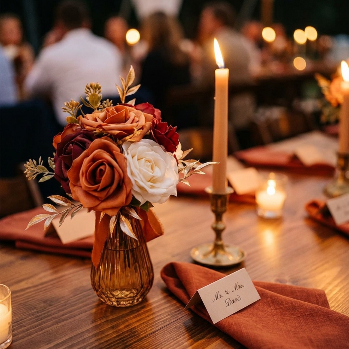 Terracotta floral arrangement in an amber glass vase on a wedding reception table at night with candlelight