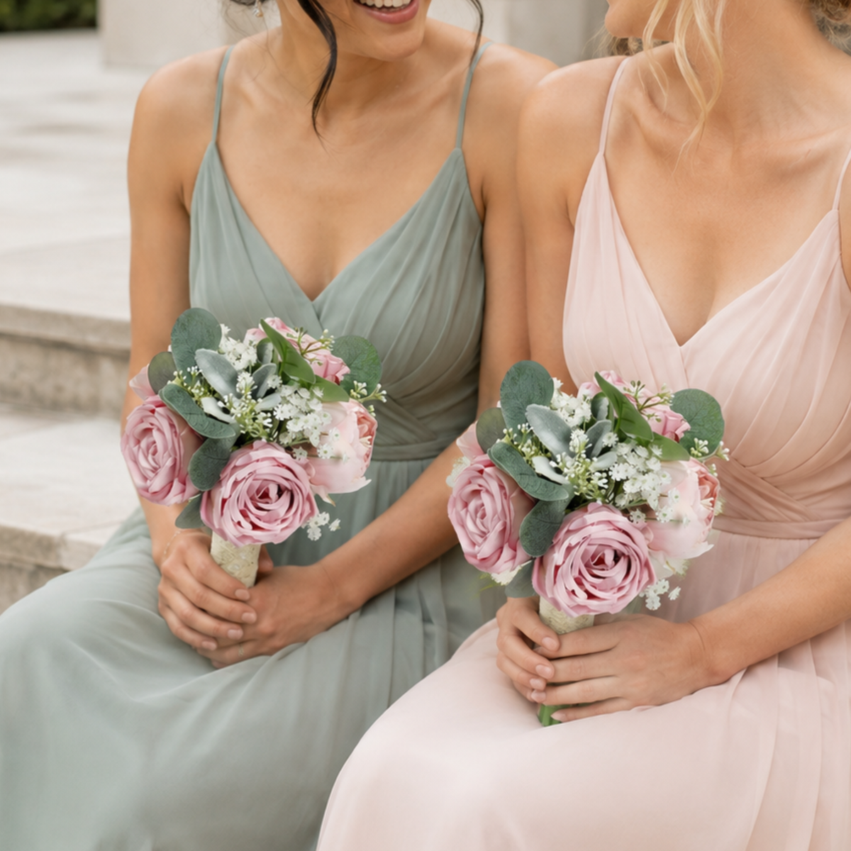 Two bridesmaids in sage green and blush dresses each holding a dusty pink peony bouquet