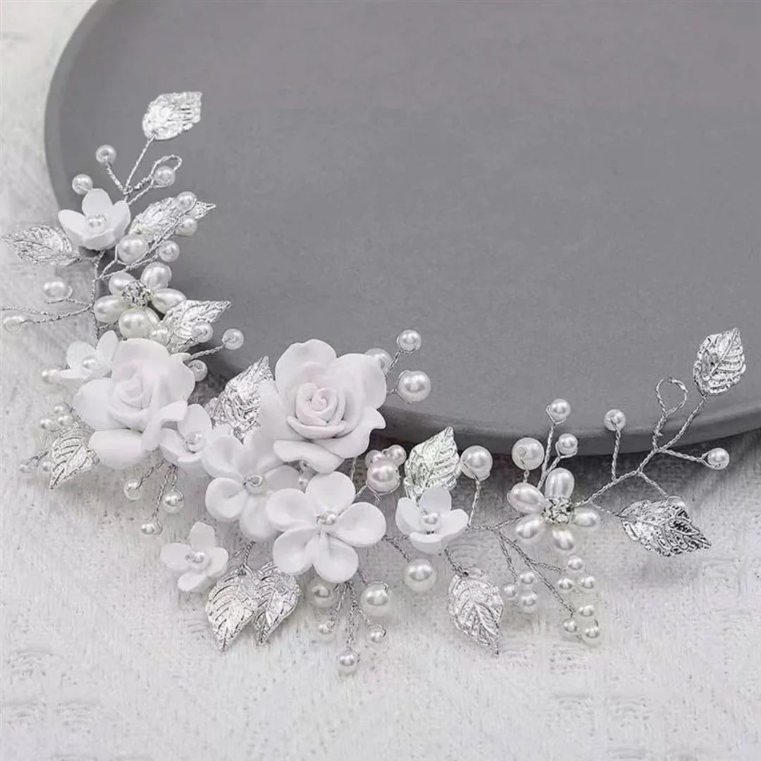 Silver bridal hair vine with white flowers, faux pearls and metal leaves laid flat on a gray surface