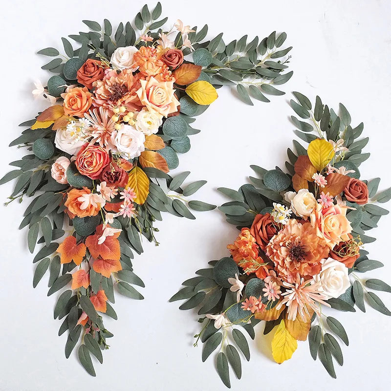 Burnt orange and peach faux rose swags with dahlias, yellow leaves and eucalyptus laid on white