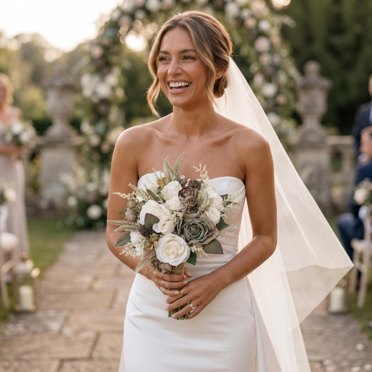 Bride in a strapless gown holding a sage and ivory artificial bouquet in an outdoor garden ceremony